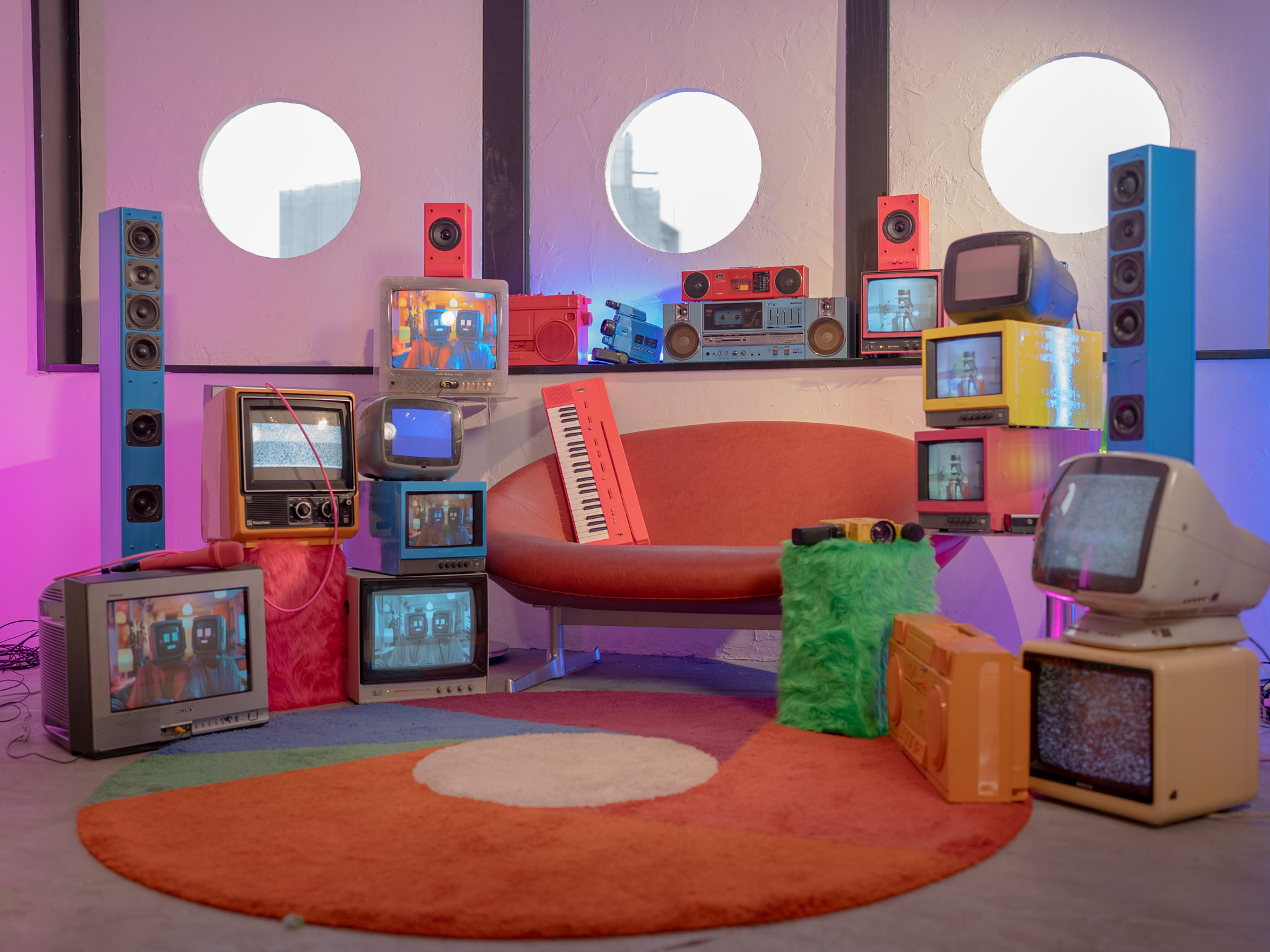 レトロポップ平和島のテレビエリア。丸窓の前にブラウン管テレビを複数配置し、カラフルなラグやソファー、小物と組み合わせたセット写真