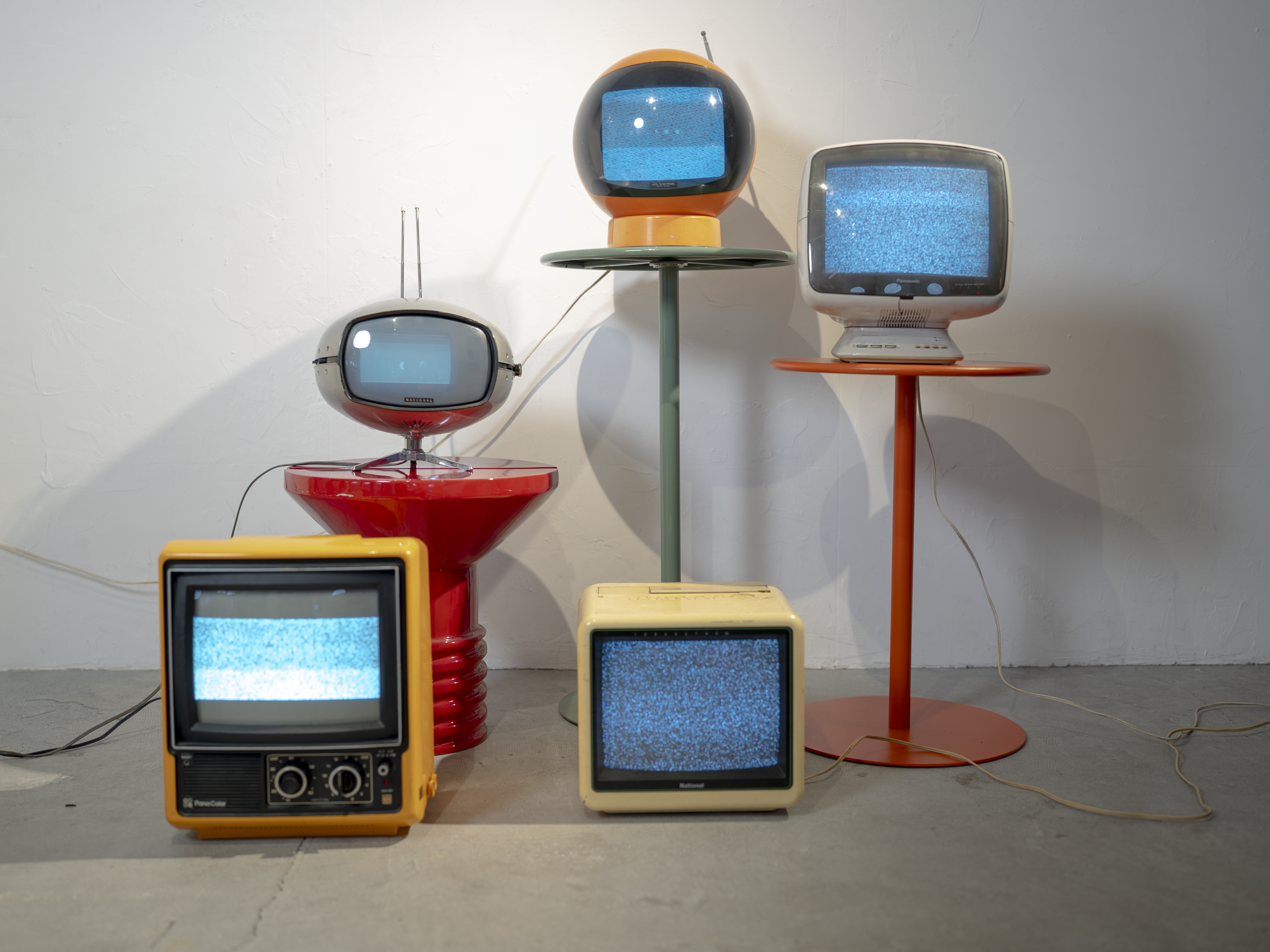 高さの違う一本足テーブルに、形や色の異なるブラウン管テレビを並べたレトロポップ平和島のセット写真