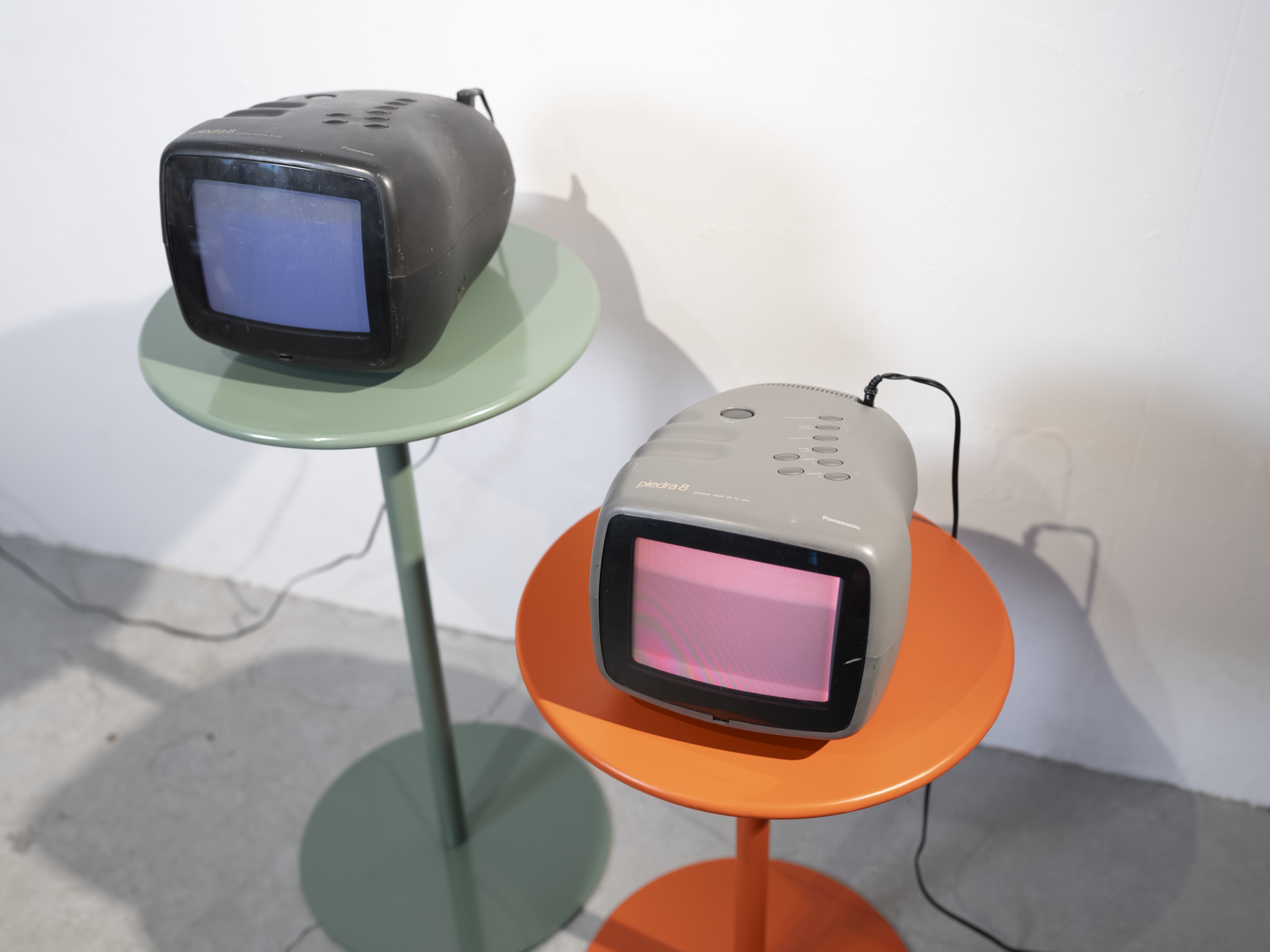 Panasonicのピエドラ(Piedra)ブラウン管テレビを2台並べた写真。丸みのある独特なフォルムのテレビを、グリーンとオレンジの一本足テーブルに載せたセット